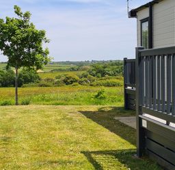 A grassy yard with a small tree and a railing of a building overlooking fields at Vendee Lodge Thorness Bay Holiday Park near Cowes