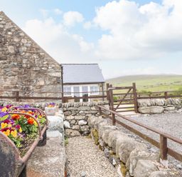 A stone building with a gravel pathway and colorful flowers in planters at Caerffynon Bach in Dyffryn Ardudwy