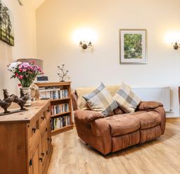 A living room with brown armchairs wooden cabinet with flower vase and bookshelf at Caerffynon Bach in Dyffryn Ardudwy