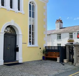 A yellow building with a dark door and tall windows next to a bench and a traffic sign at Ty Biwmares in Beaumaris