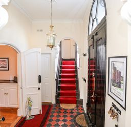 An entry hallway with a red carpeted staircase black front door a hanging light fixture and a framed picture on the wall at Ty Biwmares Beaumaris