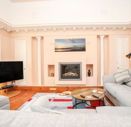 A living room with two grey sofas a round wooden coffee table a fireplace and a wall-mounted television at Ty Biwmares in Beaumaris