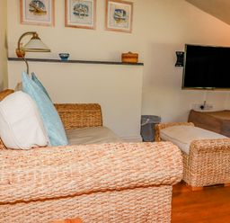 A sitting area with wicker furniture including a sofa and ottoman a wall-mounted television and framed pictures at Periwinkle Atlantic Highway near Bude
