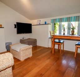 A small living area with wicker furniture a wall-mounted TV a wooden dining table with two chairs and a window with a striped blind at Periwinkle Atlantic Highway near Bude