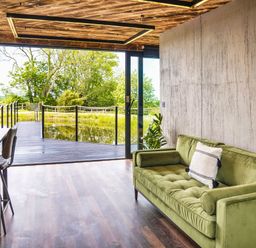 A room with a green sofa and kitchen counter with stools overlooking a deck and trees at Rusty Boathouse in Llanarth