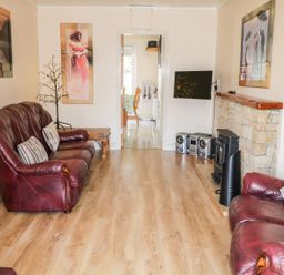 A living room with two brown leather sofas a wooden side table a wall-mounted television and a stereo system at Bridgetown Cottage in Kerrykeel County Donegal