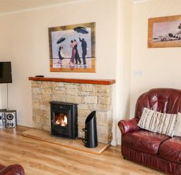 A living room with a leather sofa a fireplace with a fire a television and stereo system at Bridgetown Cottage in Kerrykeel County Donegal
