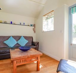 A living room with a brown leather sofa with blue cushions a wooden table with a blue bowl and a glass door at Cameo Atlantic Highway near Bude