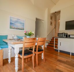 A dining area with a wooden table and chairs a built-in bench with blue cushions a TV microwave and toaster on a counter at Cameo Atlantic Highway near Bude