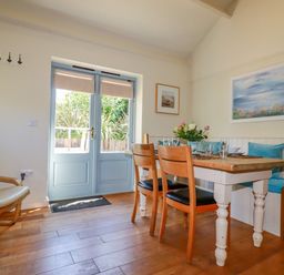 A dining area with a wooden table and chairs by blue double doors at Cameo Atlantic Highway near Bude