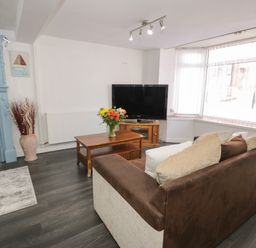 A living room with a sofa facing a television and a wooden coffee table with flowers at Penrallt in Cemaes Bay