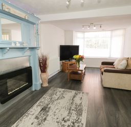 A living room with a fireplace a TV on a stand a sofa and a coffee table with flowers at Penrallt in Cemaes Bay