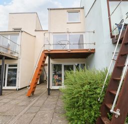 The rear view of a modern house with glass balconies wooden stairs and a bush in front at The Moorings in Porthmadog