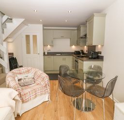A kitchen with green cabinets a glass dining table with four chairs next to a staircase and an armchair at The Moorings in Porthmadog