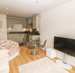 A kitchen and living room area with cabinets dining table chairs sofas and a television at The Moorings in Porthmadog