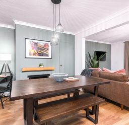 A dining area with a wooden table and bench next to a living room with a brown sofa and a wall-mounted TV at The View in Whitby