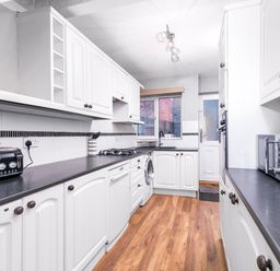 A kitchen with white cabinets black countertops and wooden floor at The View in Whitby