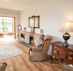 A living room with armchairs a fireplace a wooden chest with a lamp and a floral rug at Glebe Farm Cottage in Rathfriland County Down