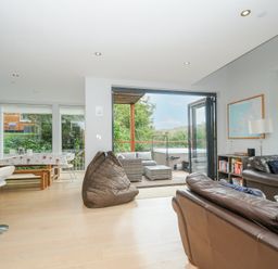 An open living room and kitchen area with brown leather sofas a bean bag dining table and chairs and a view to an outdoor patio with seating and hot tub at 9 Cedars in St Agnes
