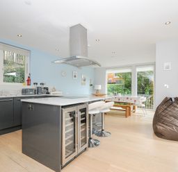 A kitchen with an island counter stools and a dining area with large windows at 9 Cedars in St Agnes