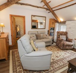 A living room with sofas armchair wooden cabinet and a patterned rug at Gull Cottage Hermon near Newborough