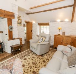 A living room with a wood stove armchairs a sofa wooden cabinet and a patterned rug at Gull Cottage in Hermon near Newborough