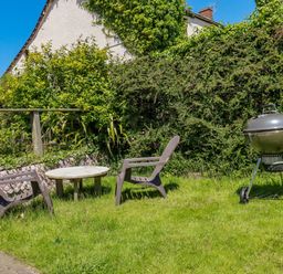 A garden with two chairs a small round table and a barbecue grill at Abalone in Bude