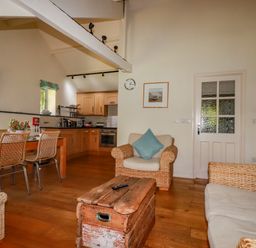 A living room and kitchen area with wicker chairs wooden table and a wooden chest at Abalone in Bude