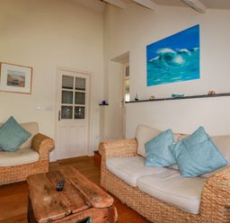 A living room with wicker armchairs and a sofa with blue cushions and a wooden coffee table at Abalone in Bude