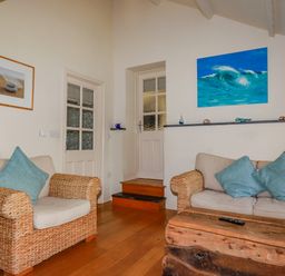 A living room with wicker armchairs with cushions wooden coffee table paintings on the walls at Abalone in Bude