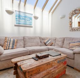 A living room with a beige corner sofa and wooden coffee table with a mirror framed with shells at Seashells Atlantic Highway near Bude