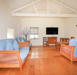 A living room with wooden sofas with blue cushions a coffee table a TV on the wall and wooden floor at Oyster Atlantic Highway near Bude