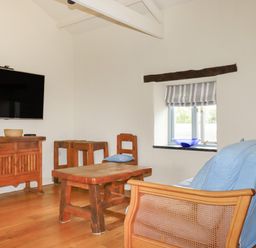 A sitting room with wooden furniture a mounted TV and a window with striped blinds at Oyster Atlantic Highway near Bude