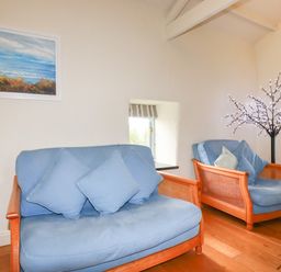 Two blue cushioned armchairs with wooden frames next to small windows in a room with wooden floor and a lighted decorative tree at Oyster Atlantic Highway near Bude