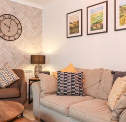 A sitting area with a beige sofa and brown armchair by a wooden coffee table and wall clock at Bluebell Hill in Bowness-On-Windermere