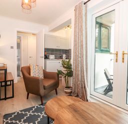 A living room with armchair coffee table and glass doors leading to a balcony at Bluebell Hill in Bowness-On-Windermere