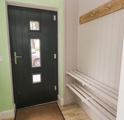 An entryway with a black door featuring three small windows a wooden coat rack with hooks and a white wooden bench at Landfall in St Twynnells near Pembroke