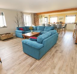An open living room with blue sofas and a wooden coffee table connected to a kitchen with bar stools at Landfall in St Twynnells near Pembroke