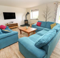 A living room with blue sofas a wooden coffee table a wall mounted TV and a wood burning stove at Landfall in St Twynnells near Pembroke