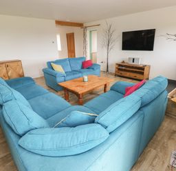A living room with blue sofas wooden coffee table and cabinet with a wall mounted tv at Landfall in St Twynnells near Pembroke