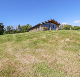 A wooden cottage on a grassy hill with trees in the background at Atlantic Lodge Atlantic Highway near Bude