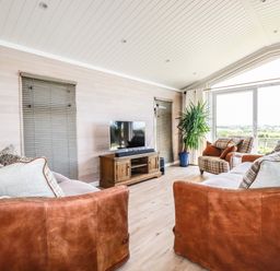 A living room with leather sofas a wooden TV stand indoor plants and large windows at Atlantic Lodge Atlantic Highway near Bude