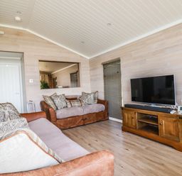 A living room with two sofas a wooden TV cabinet a flat-screen TV and a speaker at Atlantic Lodge Atlantic Highway near Bude