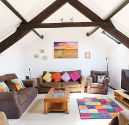 A sitting room with sofas colorful cushions a coffee table a multicolored rug a television and exposed wooden beams at The Corn Tallet in Westleigh near Bideford