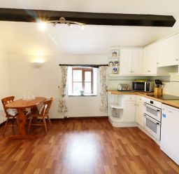 A kitchen with wooden flooring a dining table with chairs and white cabinets at The Corn Tallet in Westleigh near Bideford