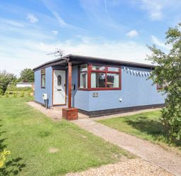 A blue single-story building with a white door and windows surrounded by grass and small bushes at Rollin Dunes in Humberston Lincolnshire