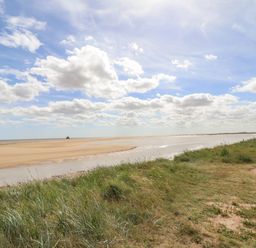 A sandy beach with water and grassy area with a bench near the shore at Rollin Dunes in Humberston Lincolnshire