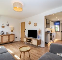 A living room with a grey sofa wooden sideboards a TV and an open door to the kitchen at Rollin Dunes in Humberston Lincolnshire
