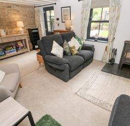 A living room with a sofa and armchair near a wood stove and a console table with board games at Wood Brook Cottage in Crowan