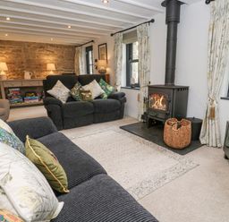 A living room with sofas cushions a wood burning stove and a console with board games at Wood Brook Cottage in Crowan